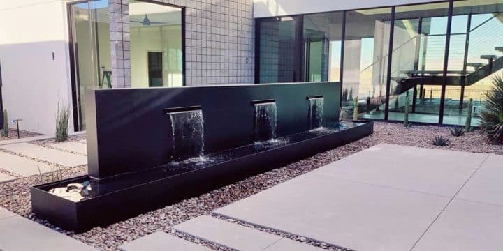 Modern black wall water fountain with three spouts cascading into a trough to mask outdoor street noise effectively.